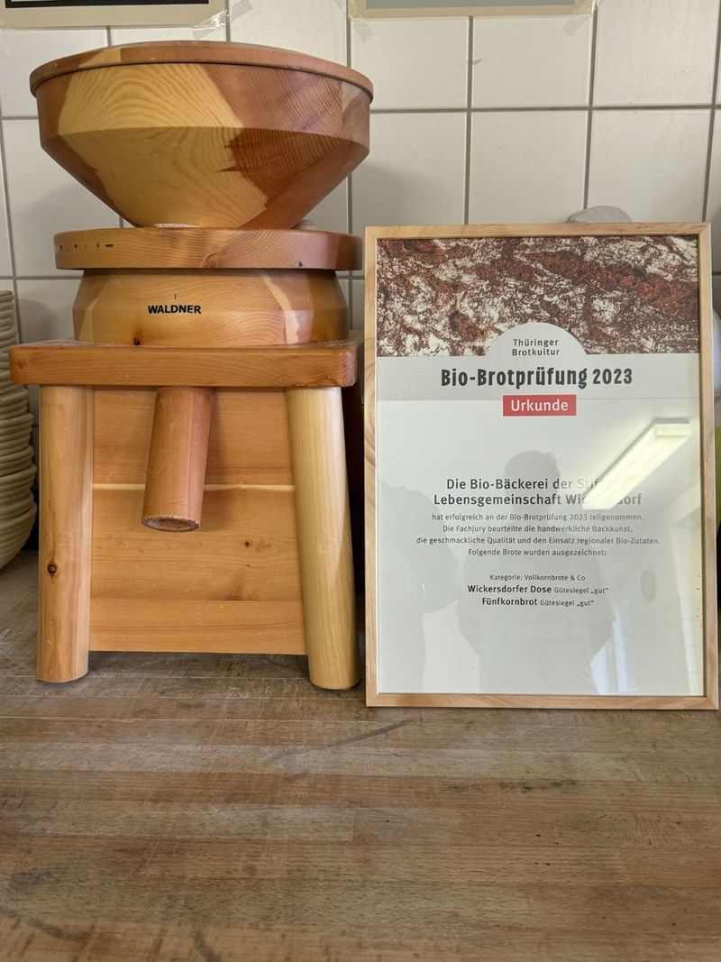 Hölzerne Getreidemühle neben gerahmter Urkunde der Bio-Brotprüfung 2023