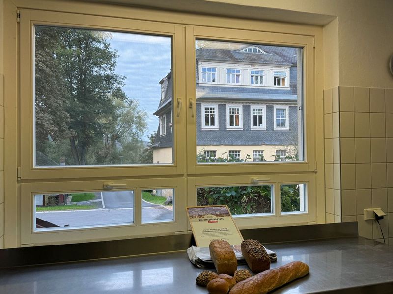 Frische Brote auf der Arbeitsfläche vor dem Backstubenfenster mit Blick auf ein Schieferhaus