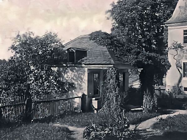 Historische Aufnahme: kleines, von Kletterpflanzen bewachsenes Haus mit Lattenzaun und Garten