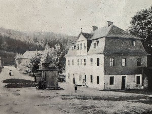 Historische Aufnahme: Dorfplatz mit großem Mansarddachhaus, kleinem Pavillon und Torpfeilern