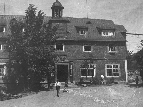 Historische Aufnahme: großes Schieferhaus mit Dachreiter, davor ein Hof mit einigen Personen
