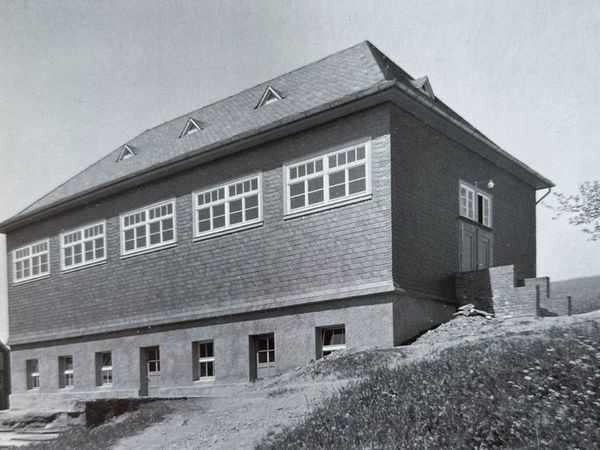 Historische Aufnahme: großer Neubau mit Walmdach und langen Fensterreihen am Hang