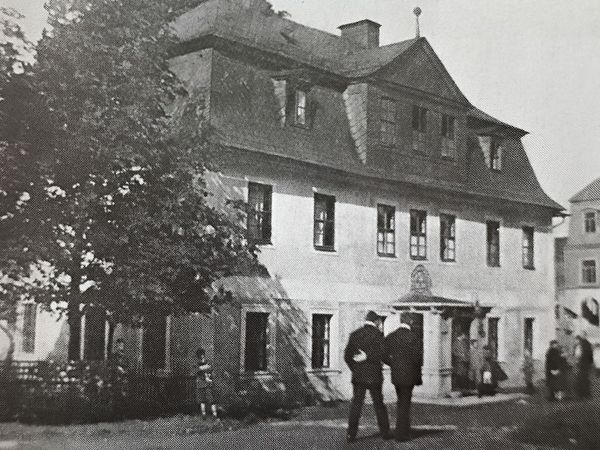 Historische Aufnahme: Herrenhaus mit Mansarddach und Portalvorbau, davor Männer mit Hüten