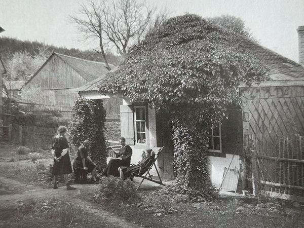 Historische Aufnahme: efeubewachsenes Häuschen, davor Menschen in Liegestühlen im Garten