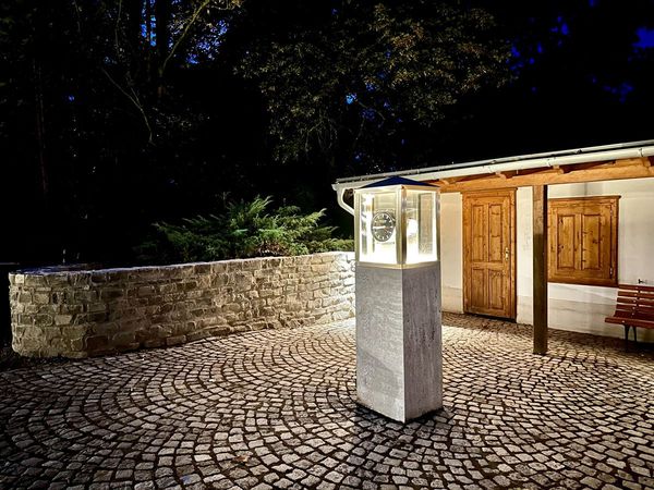 Backhaus mit beleuchteter Uhrensäule auf dem gepflasterten Platz bei Nacht