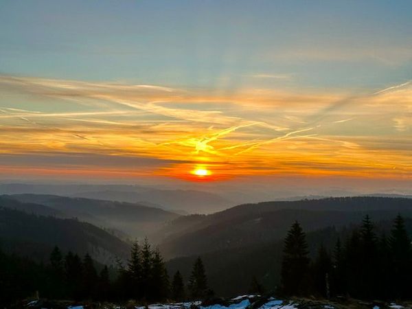 Sonnenuntergang über bewaldeten Höhenzügen und Tälern