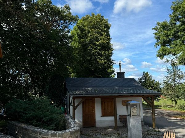 Backhaus mit Uhrensäule und Sitzbänken unter blauem Himmel mit Schäfchenwolken