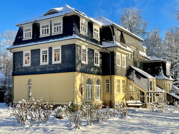 Großes Haus mit Schieferfassade und gelbem Erdgeschoss im Schnee unter blauem Himmel