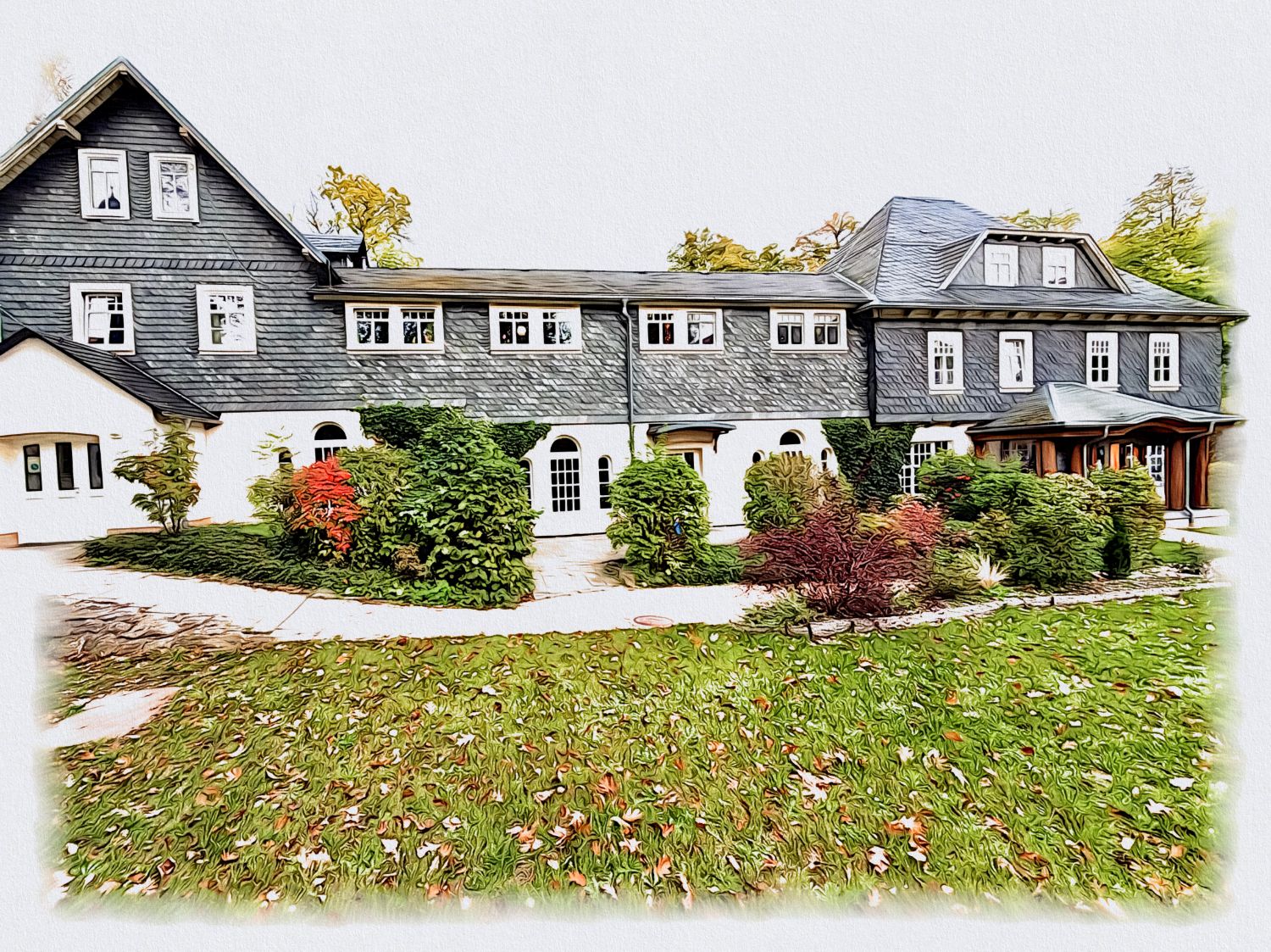 Gemaltes langgestrecktes Haus mit Schieferfassade und weißem Erdgeschoss, davor herbstliche Sträucher und Rasen mit Laub